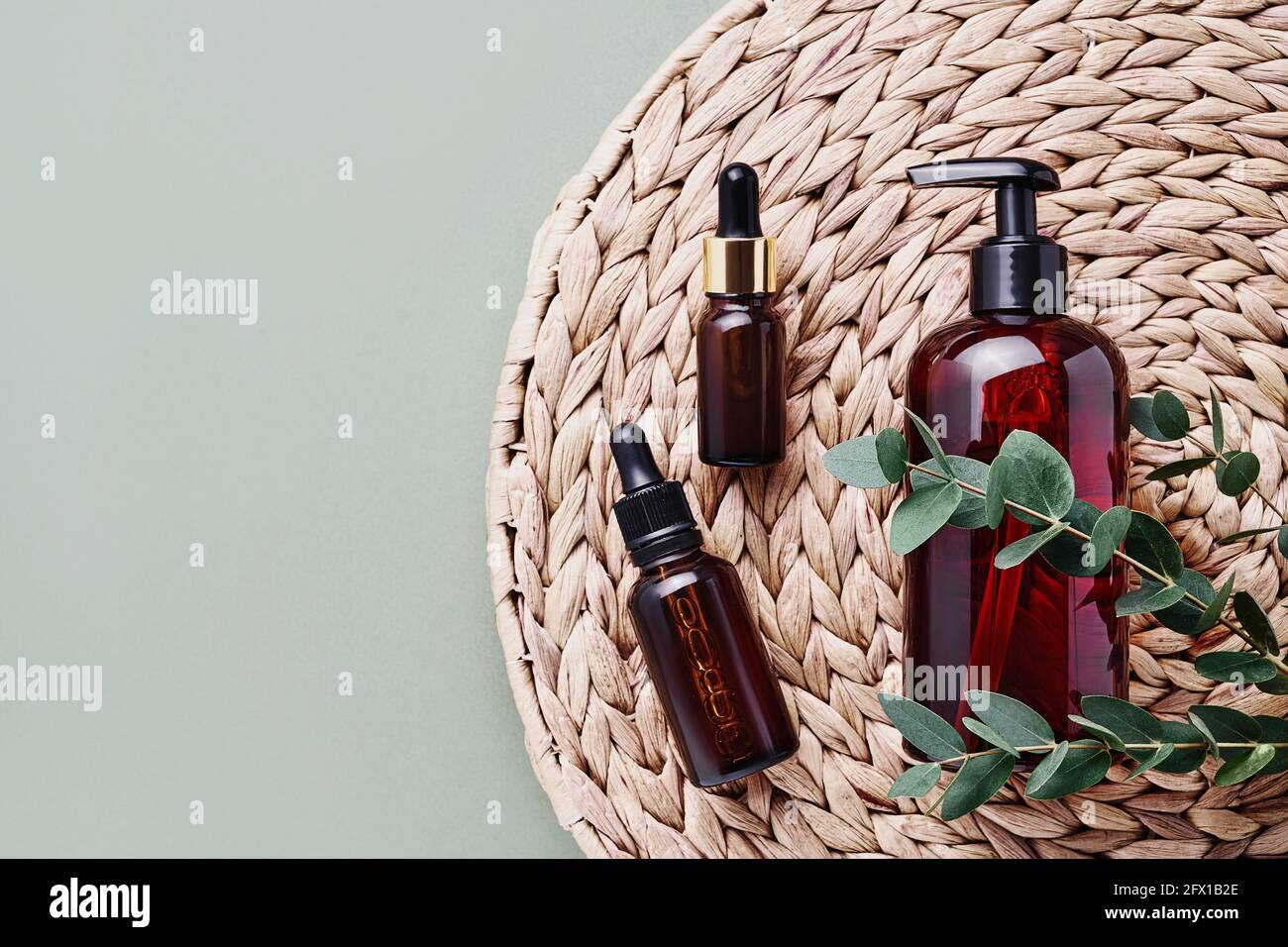 Dropper bottles of essential oil or serum, eucalyptus branches and dark dispenser bottle of shower gel on rattan background. Beauty and SPA concept. F Stock Photo