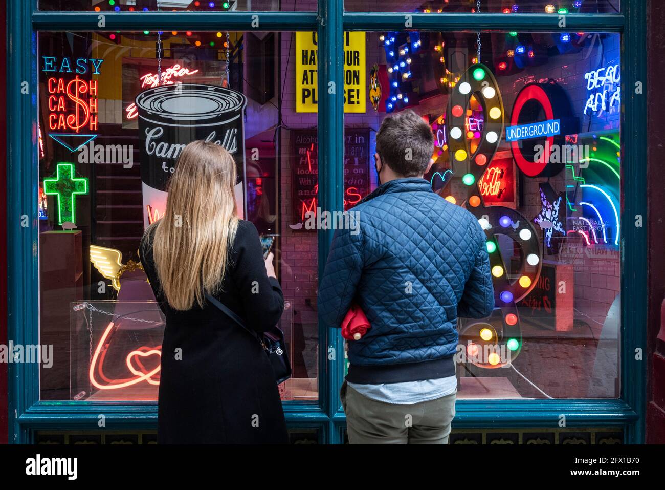 London, UK.  25 May 2021. Passers by view “Electric City” an exhibition in Leadenhall Market of neon and set pieces made for film by Gods Own Junkyard, which has worked on film sets for over 40 years. Founder, Chris Bracey passed away in 2014 and the business has since been run by his wife Linda and sons Matthew and Marcus, all neon makers and designers. On show 26th May to 31st July is neon signage from Stanley Kubrick’s Eyes Wide Shut, Judge Dredd, Batman, Tomb Raider, Charlie and the Chocolate Factory and The Dark Knight.  Credit: Stephen Chung / Alamy Live News Stock Photo