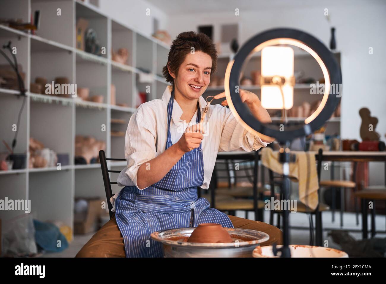 Potter showing loop tool at mobile phone near pottery wheel Stock Photo