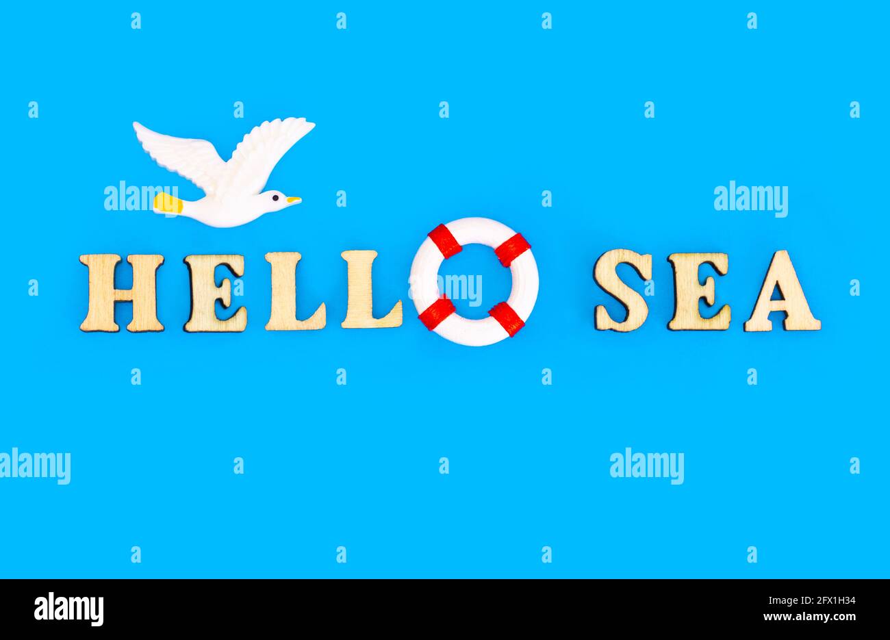 HELLO SEA composition made of wooden letters arranged on blue background with a flying toy seagull above Stock Photo
