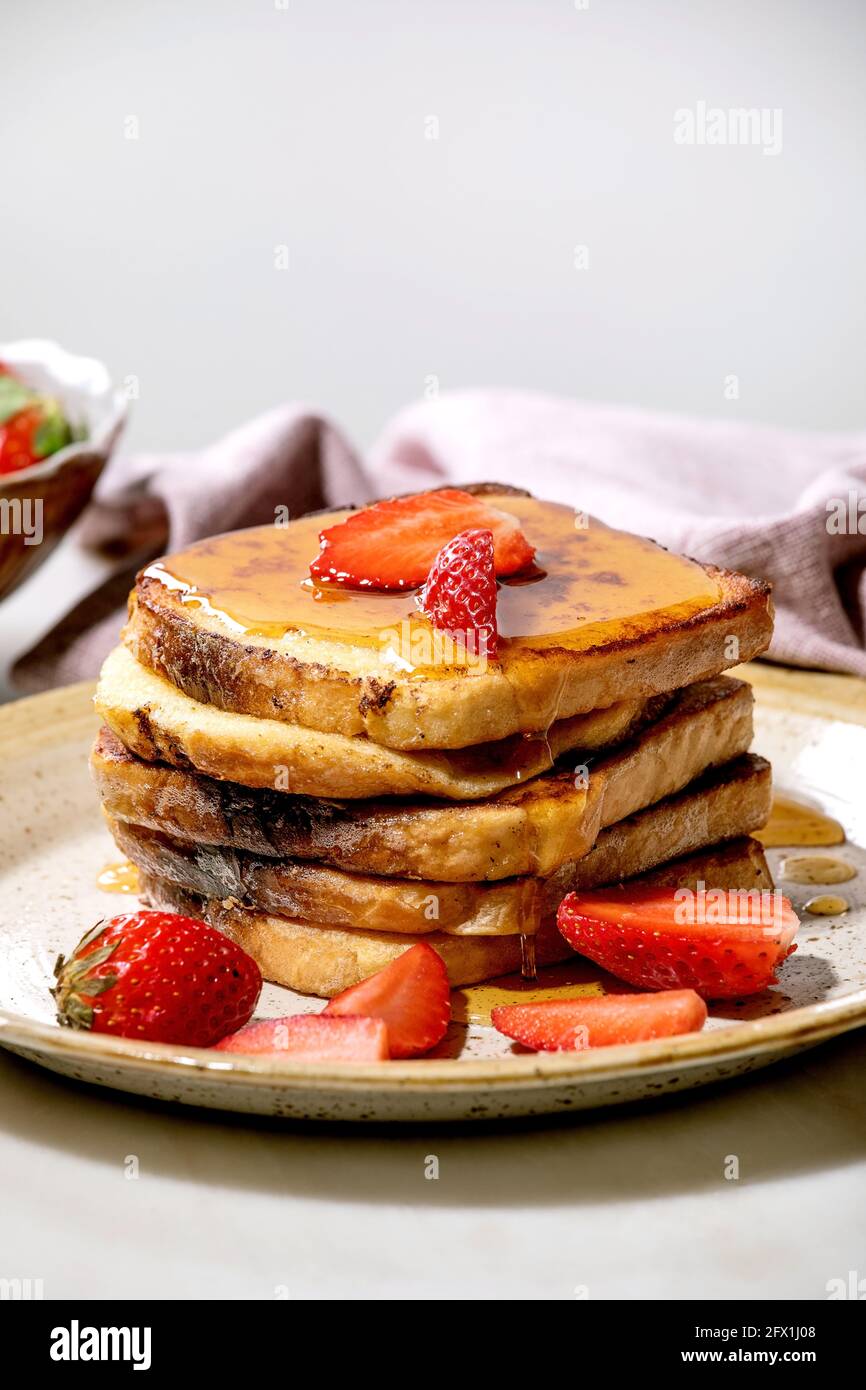 Stockpile of french toasts with fresh strawberries and maple syrup dip on ceramic plate, and pink cloth napkin over white table. Home breakfast Stock Photo