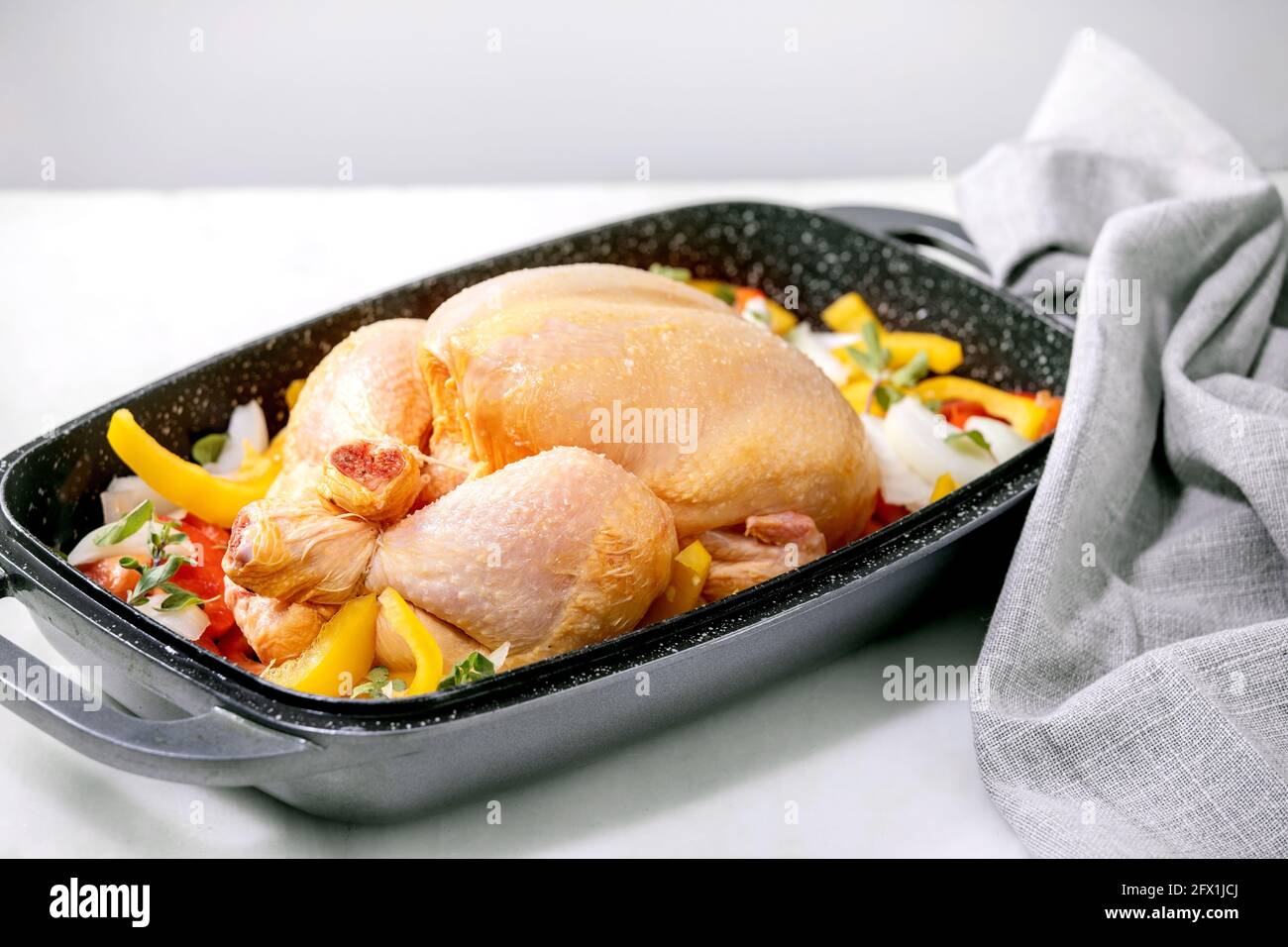 Raw organic uncooked whole chicken with sliced vegetables bell pepper, onion and herbs in oven tray with grey textile napkin, ready to cook. White mar Stock Photo