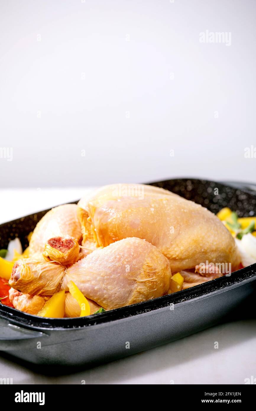 Raw organic uncooked whole chicken with sliced vegetables bell pepper, onion and herbs in oven tray, ready to cook. White marble table. Copy space Stock Photo