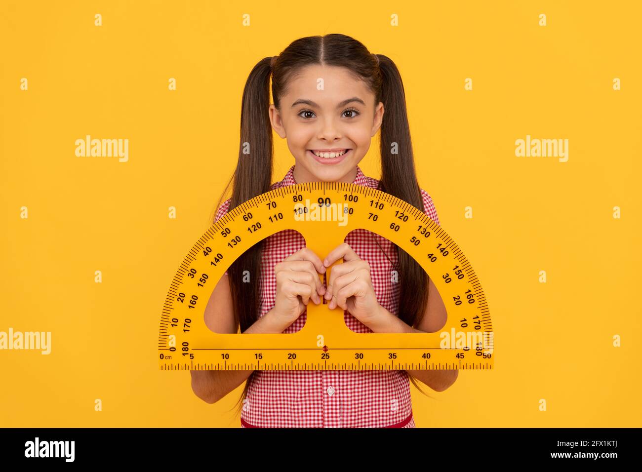 happy teen girl hold school math tool protractor ruler on yellow background, geometry Stock Photo