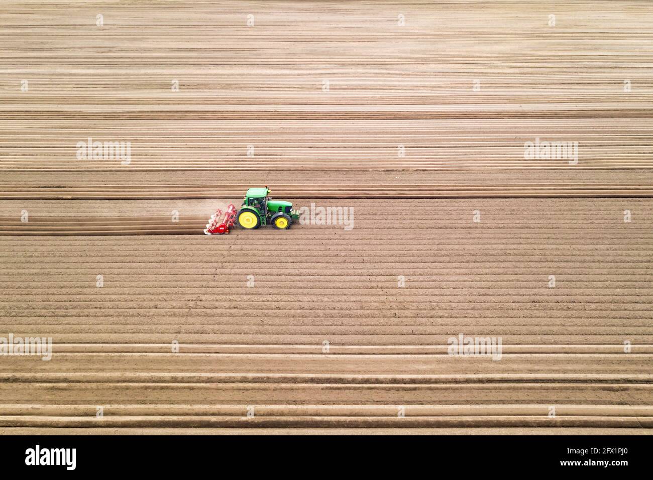 Lonely tractor on agricultural field with rows of plowed soil. Agricultural fields prepared for planting crops, topdown view. Industrial agriculture concept. Drone photography Stock Photo