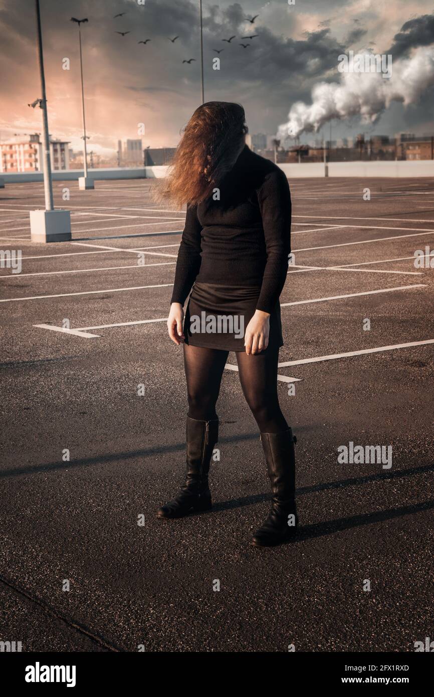 young brunette woman covering her face with her hair standing at empty ...