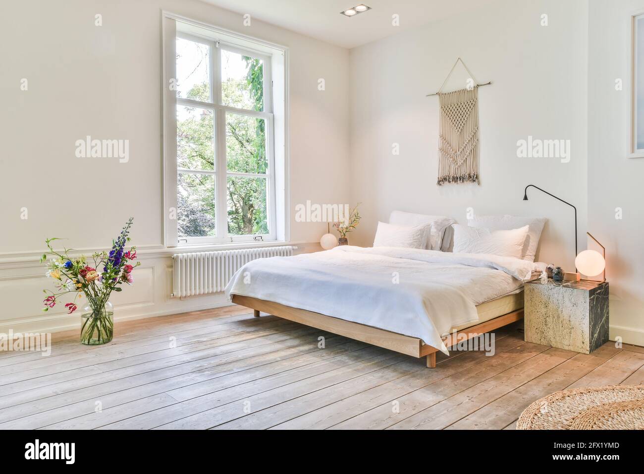 Simple bed with white linen in spacious bedroom with white walls and