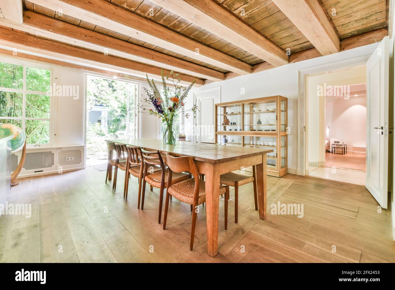 Wooden dining table with chairs under ceiling with wooden beams in cozy country room of house Stock Photo