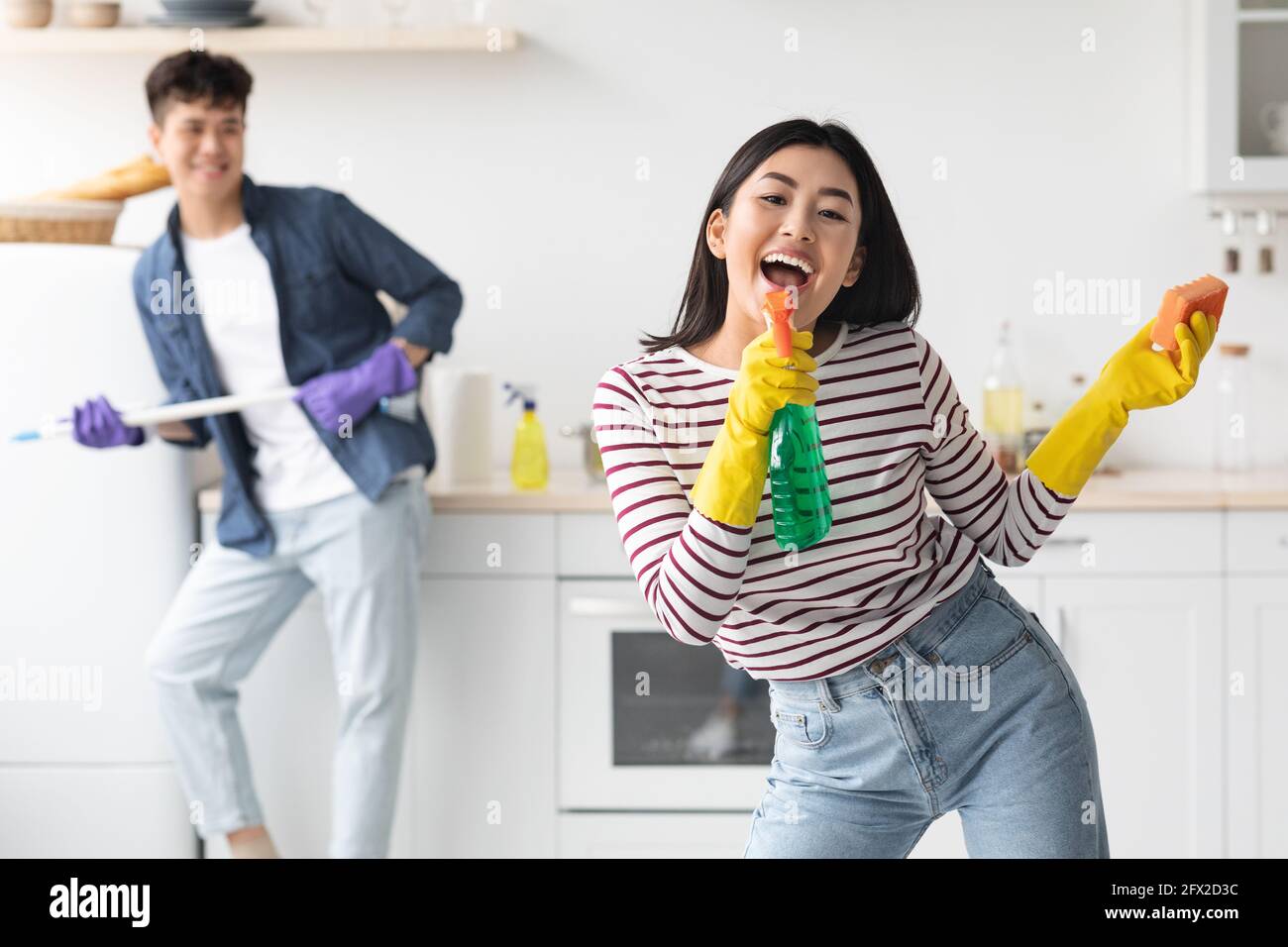 Joyful asian lady using spray as microphone, singing while cleaning Stock Photo
