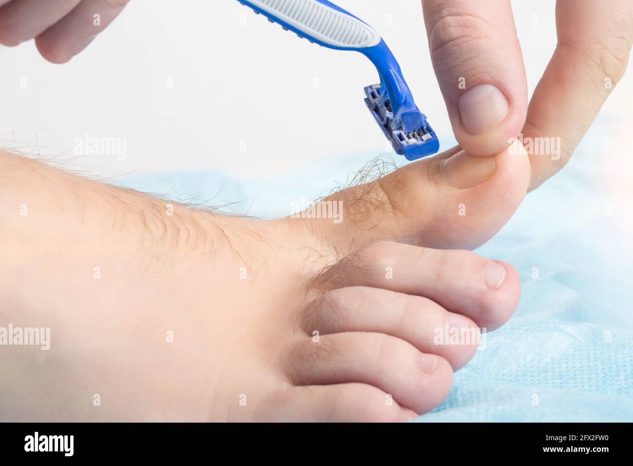 A man holds a razor near his toes where hair grows. Concept for shaving