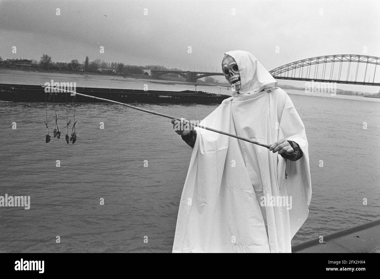 Grim Reaper with fishing rod dead fish at bank of river Waal in Nijmegen on  day of action against increasing pollution of Rhine, December 14, 1986,  demonstrations, The Netherlands, 20th century press