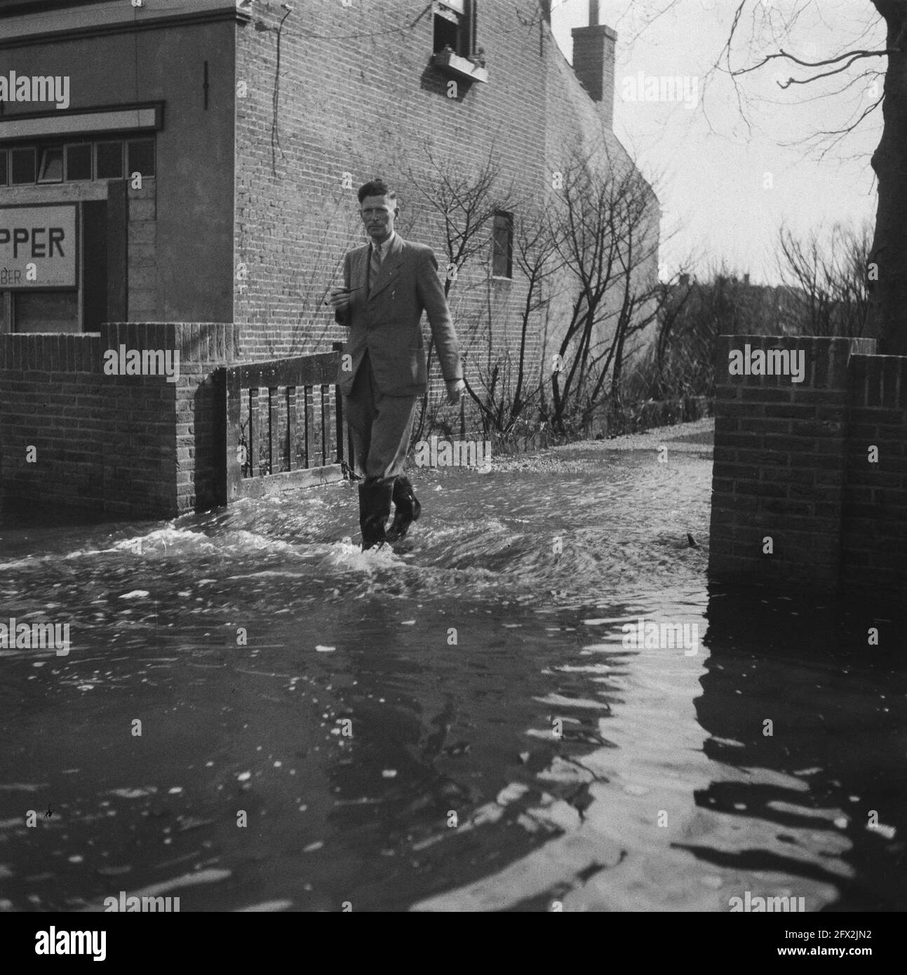 Man with boots walks down a flooded driveway, 1945, recovery, World War II, reconstruction, The Netherlands, 20th century press agency photo, news to remember, documentary, historic photography 1945-1990, visual stories, human history of the Twentieth Century, capturing moments in time Stock Photo