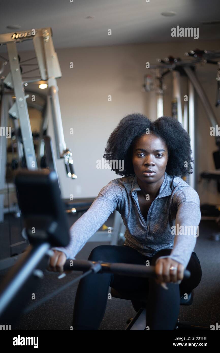 Fit young black woman working out on rowing machine, one person, natural hair model, african american, rowing machine, sportswear background, close up Stock Photo