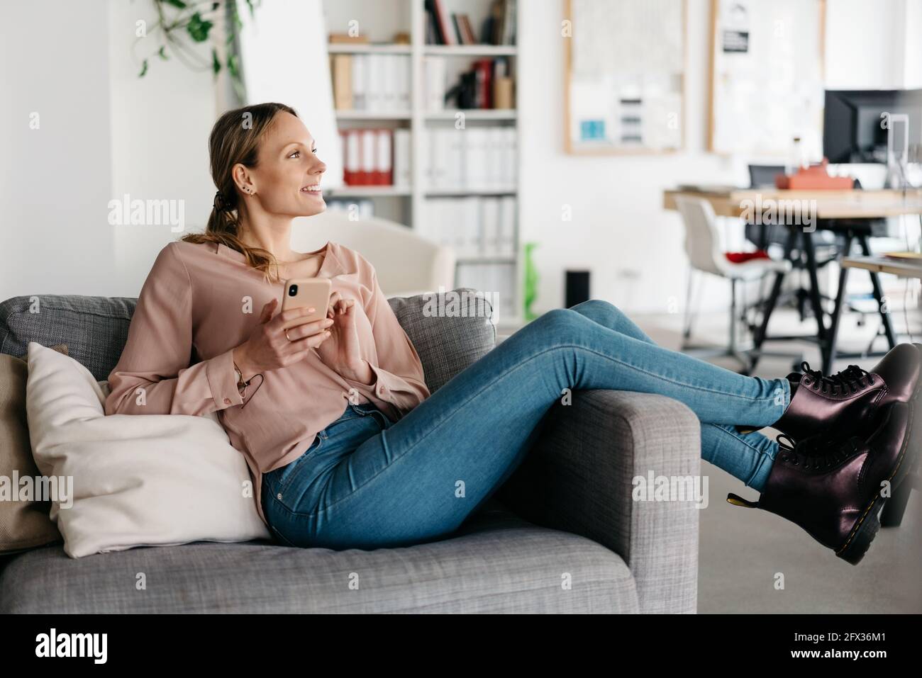 Trendy young woman in black leather boots relaxing on a sofa with her feet  up looking to the side with a happy smile and intrigued look watching Stock  Photo - Alamy