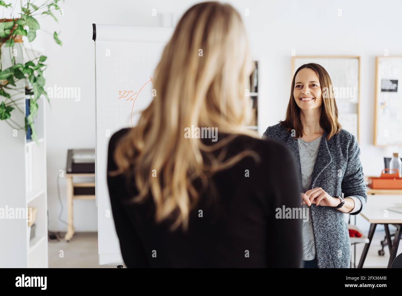 Two happy business partners or team colleagues having a discussion alongside a flip board with chart in a high key office in an over the shoulder view Stock Photo