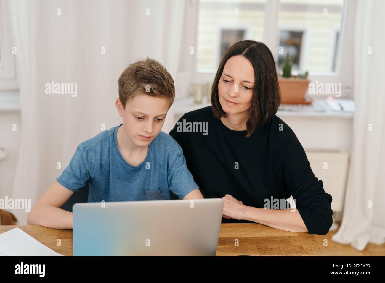 Mother helping her son with his studies on a laptop computer at home during the forced lockdown for the Coronavirus or Covid-19 pandemic Stock Photo