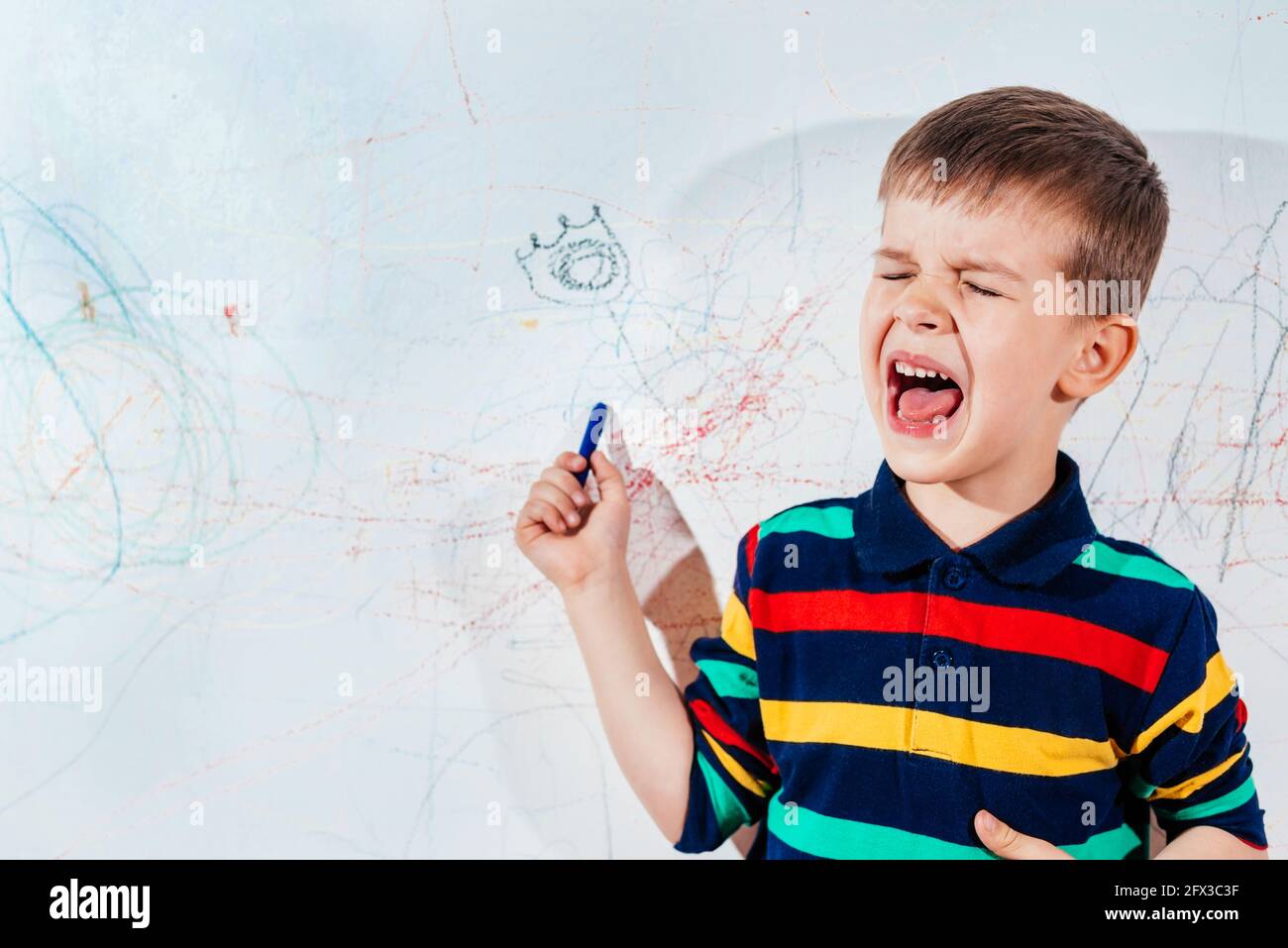 Crying child draws on the wall with crayons Stock Photo