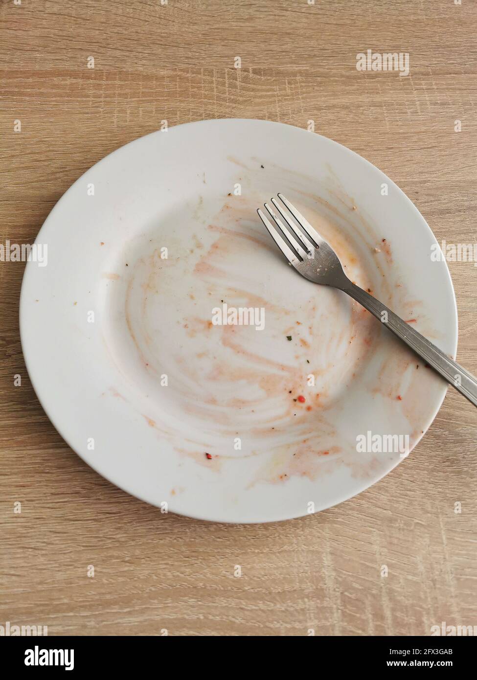 Dirty empty plate and fork after dinner on wooden table Stock Photo