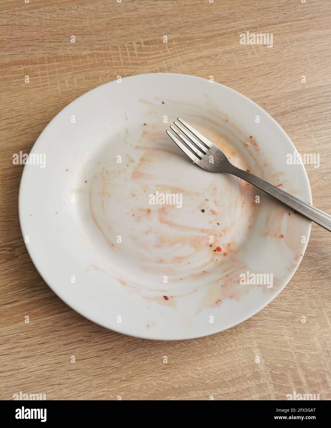 Dirty empty plate and fork after dinner on wooden table Stock Photo