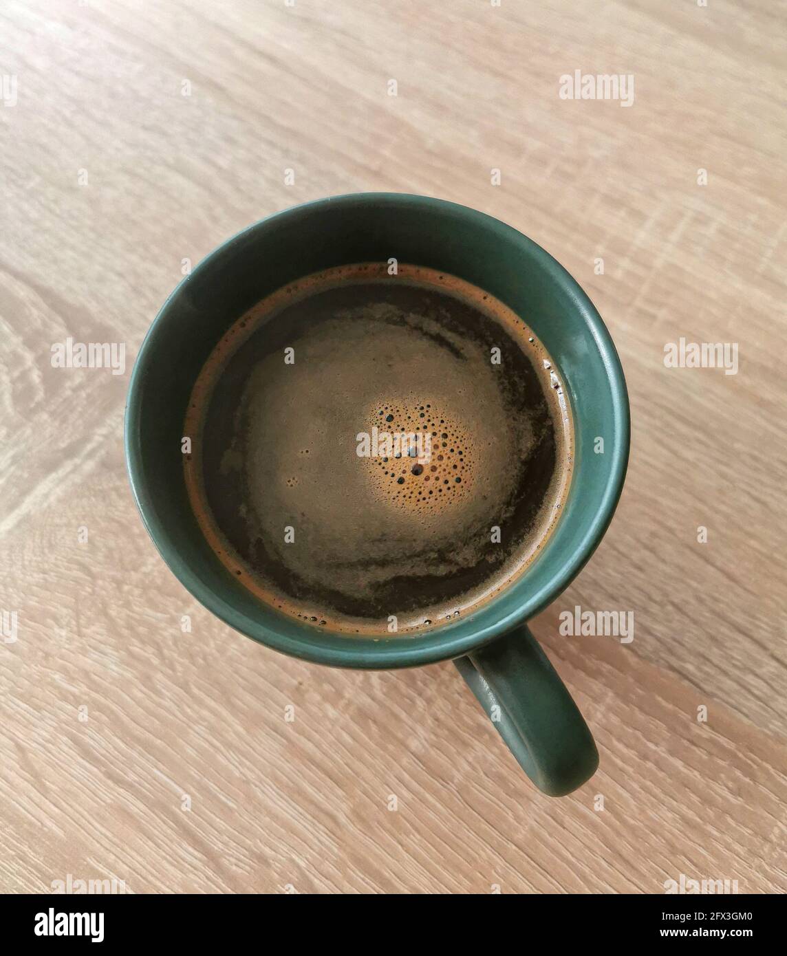 Top view of green cup of black coffee with some bubbles on a wooden table Stock Photo