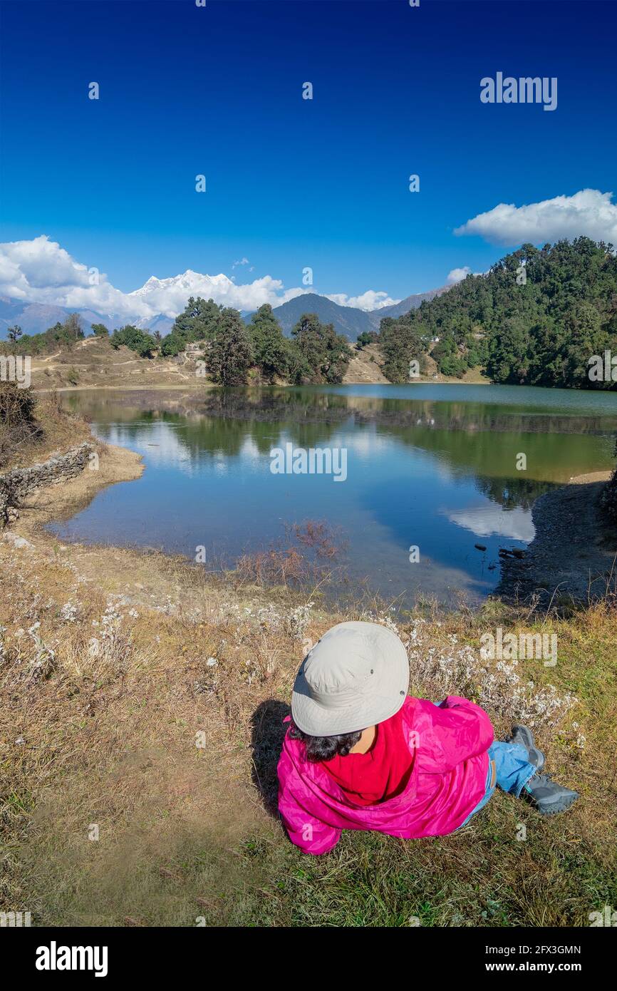 Solo traveller, single female tourist enjoying beauty of Deoria Tal while lying on green grass, high altitude lake in Uttarakhand, India. Snow-covered Stock Photo