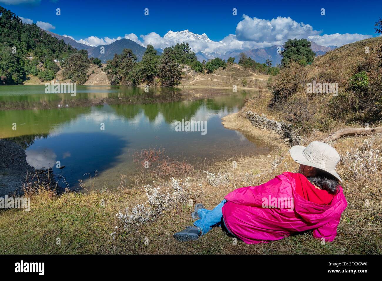 Solo traveller, single female tourist enjoying beauty of Deoria Tal while lying on green grass, high altitude lake in Uttarakhand, India. Blue sky wit Stock Photo