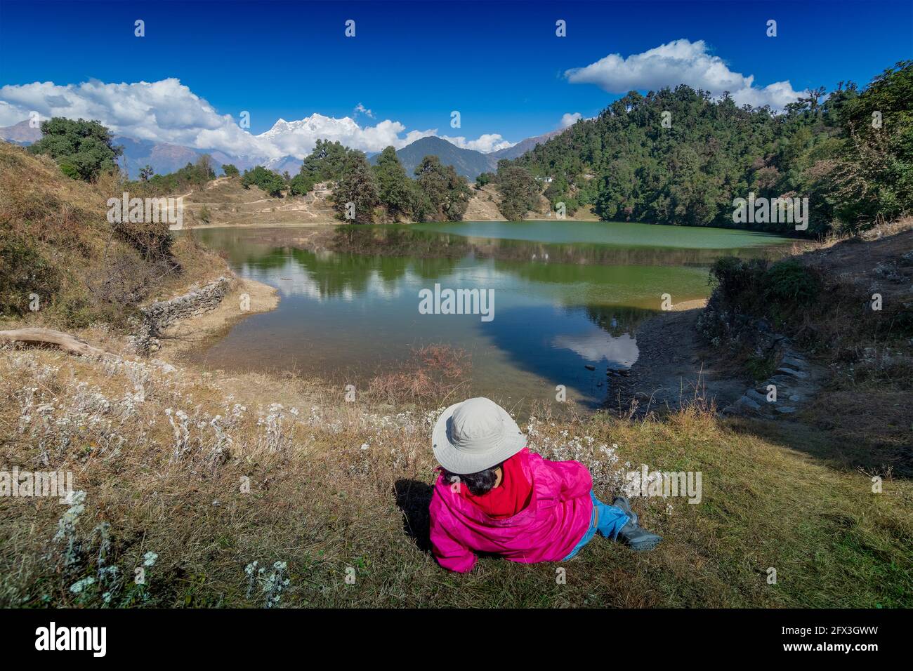 Solo traveller, single female tourist enjoying beauty of Deoria Tal while lying on green grass, high altitude lake in Uttarakhand, India. Blue sky wit Stock Photo