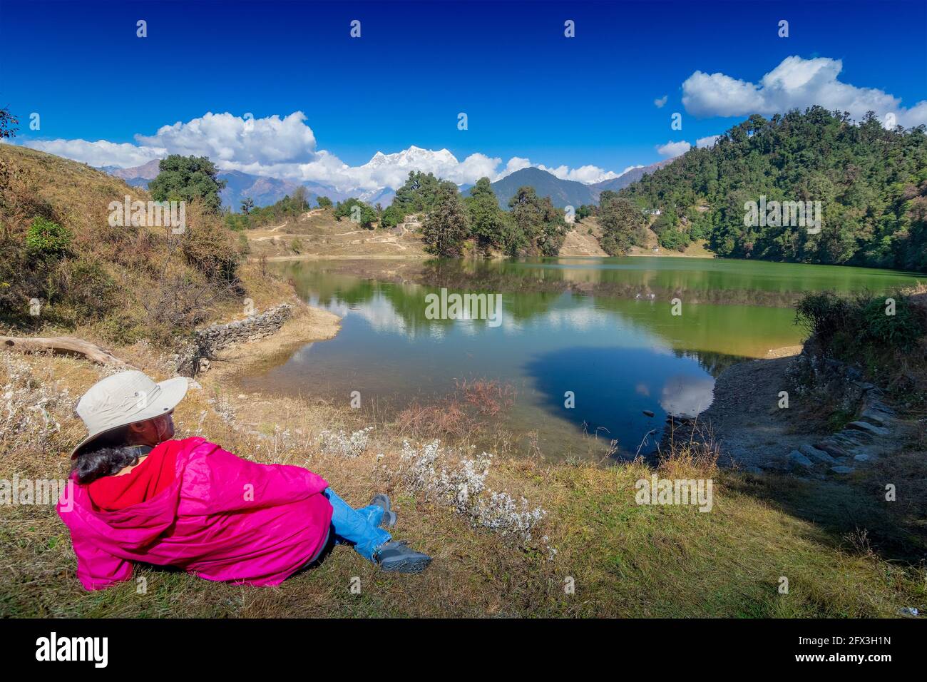 Solo traveller, single female tourist enjoying beauty of Deoria Tal while lying on green grass, high altitude lake in Uttarakhand, India. Blue sky wit Stock Photo