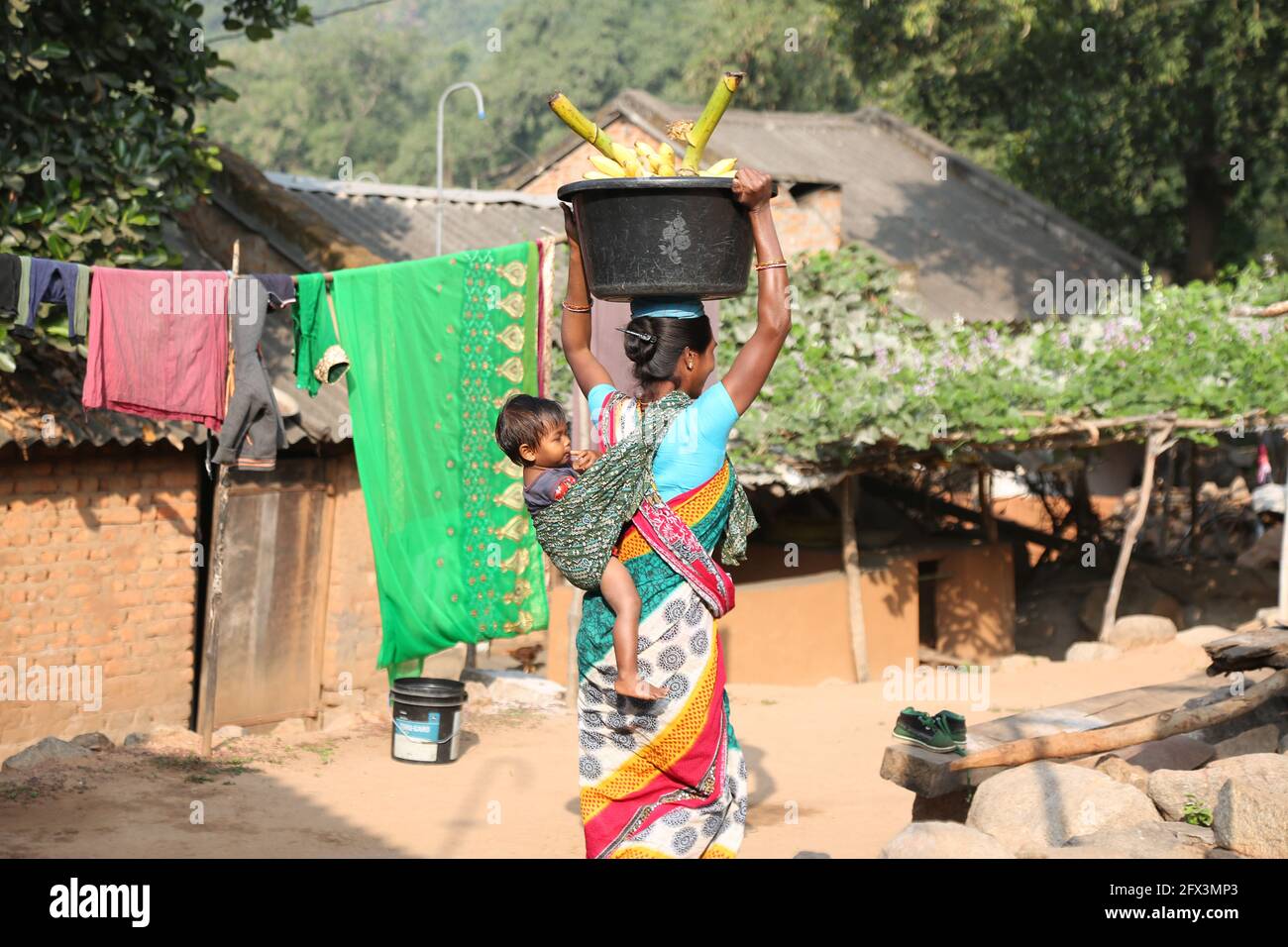 LANJIA SAORA TRIBE. Tribal woman going to village market with her baby which is tied by her sari pallu on her back. Riginghtal village, Odisha, India Stock Photo