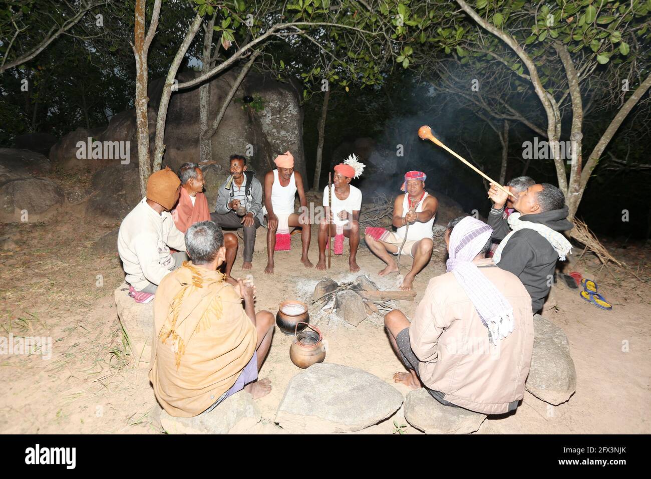 LANJIA SAORA TRIBE - Men gather in a circle drinking tadi or toddy a local wine from a large pot set over the fire. They use Jeri pipe made of dry gou Stock Photo