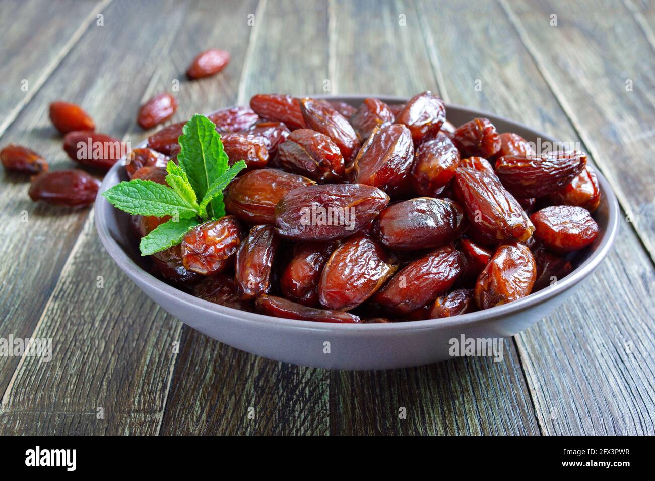 Sun-dried dates in a ceramic bowl and fruits scattered on a wooden table. Organic dried fruits. Stock Photo