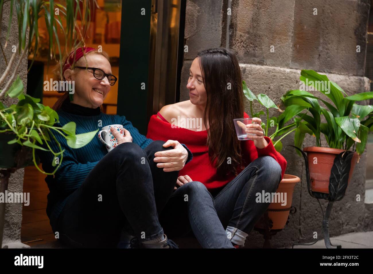 Two middle-aged female entrepreneurs sitting close together in the entrance of their shop. Concept: female entrepreneur, female friendship Stock Photo