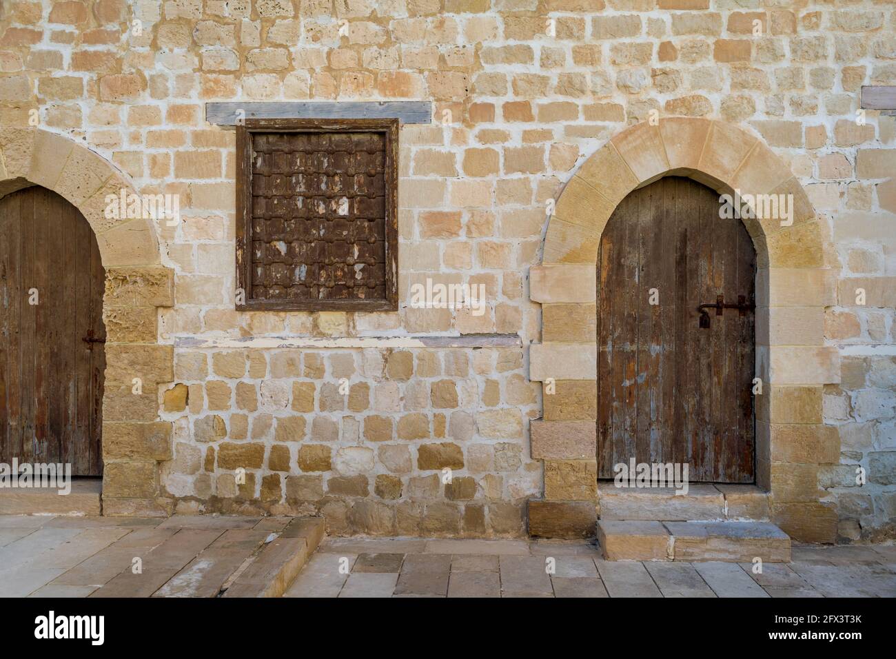 Two weathered wooden arched doors and one closed rusted wrought iron