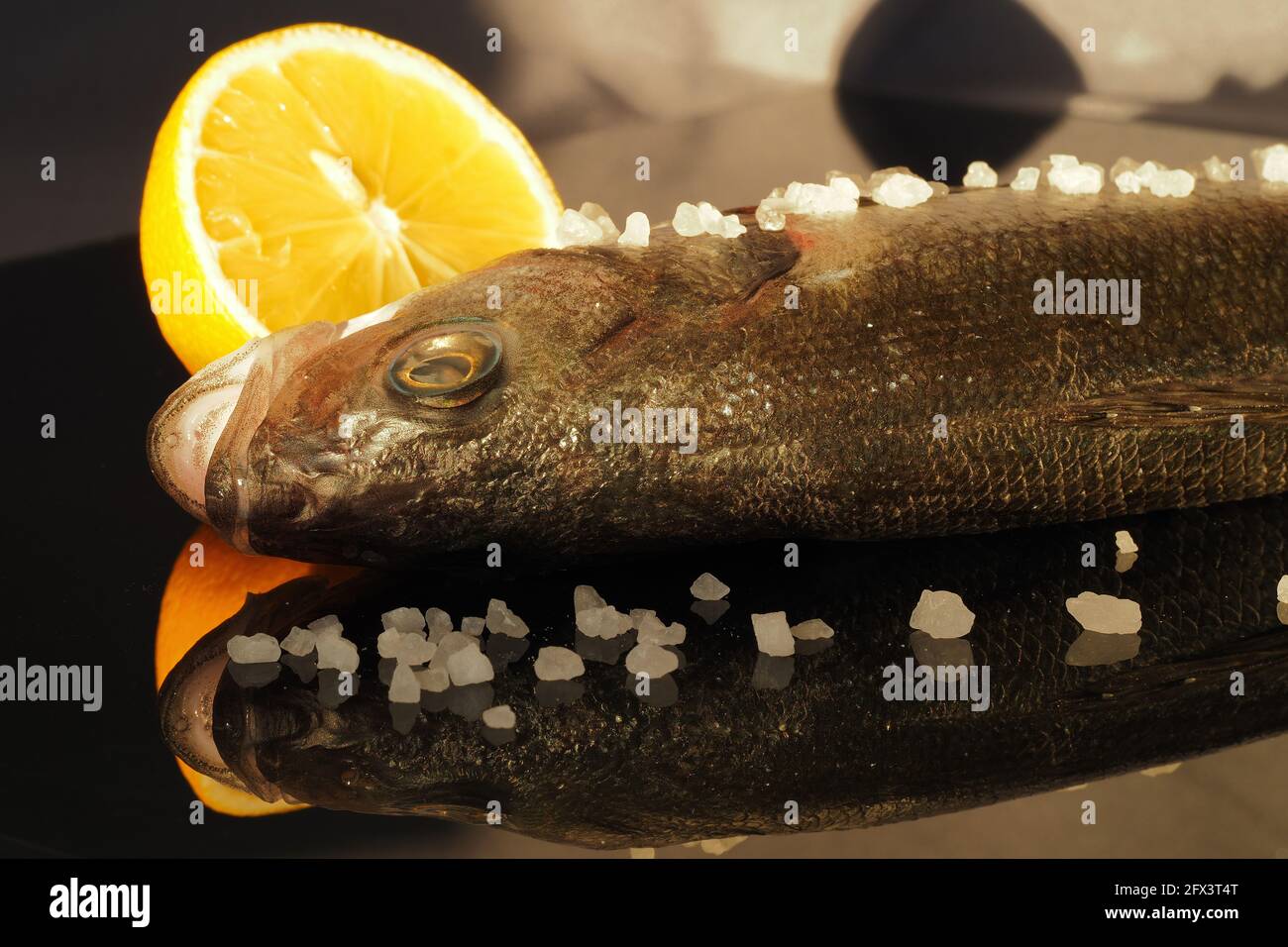 Seabass fish close-up with lemon on a glass reflective surface. Stock Photo