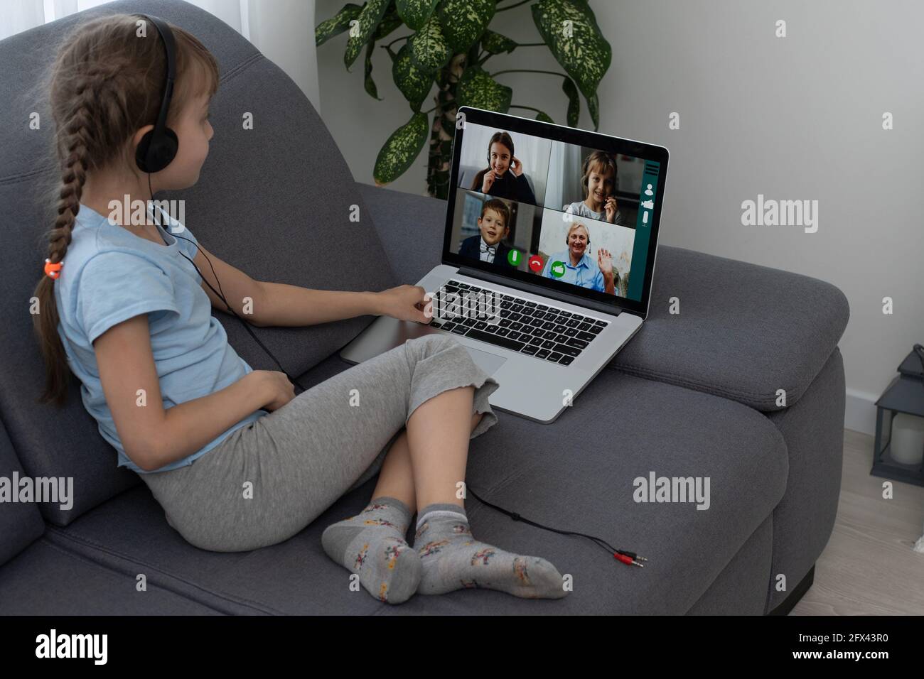 Distance learning. Cheerful little girl girl in headphones using laptop ...