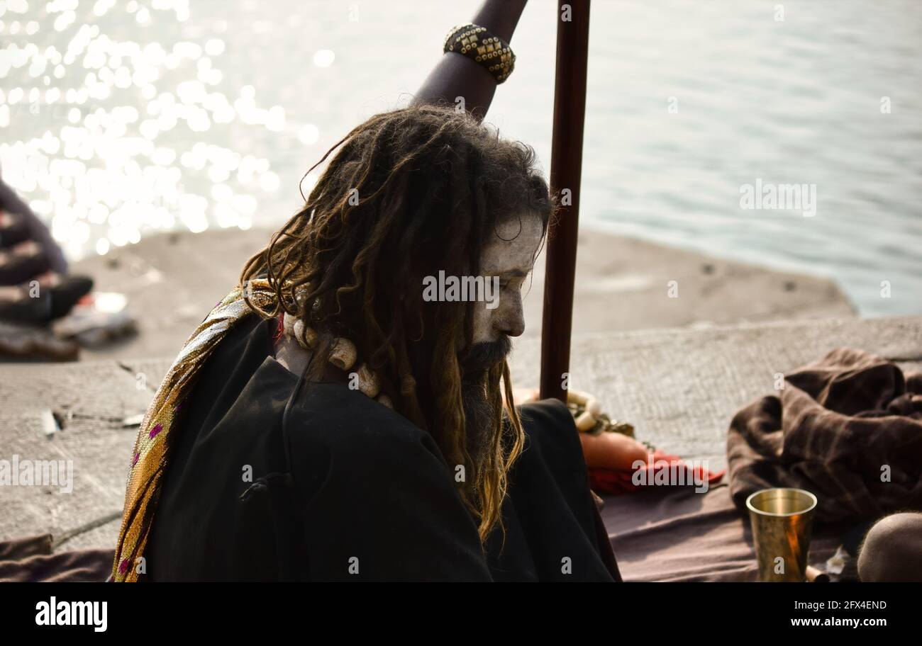 Varanasi, India - November 01, 2016: Side profile of a hindu bearded sadhu, pilgrim or Aghori baba with closed eyes sitting with a stick against gange Stock Photo