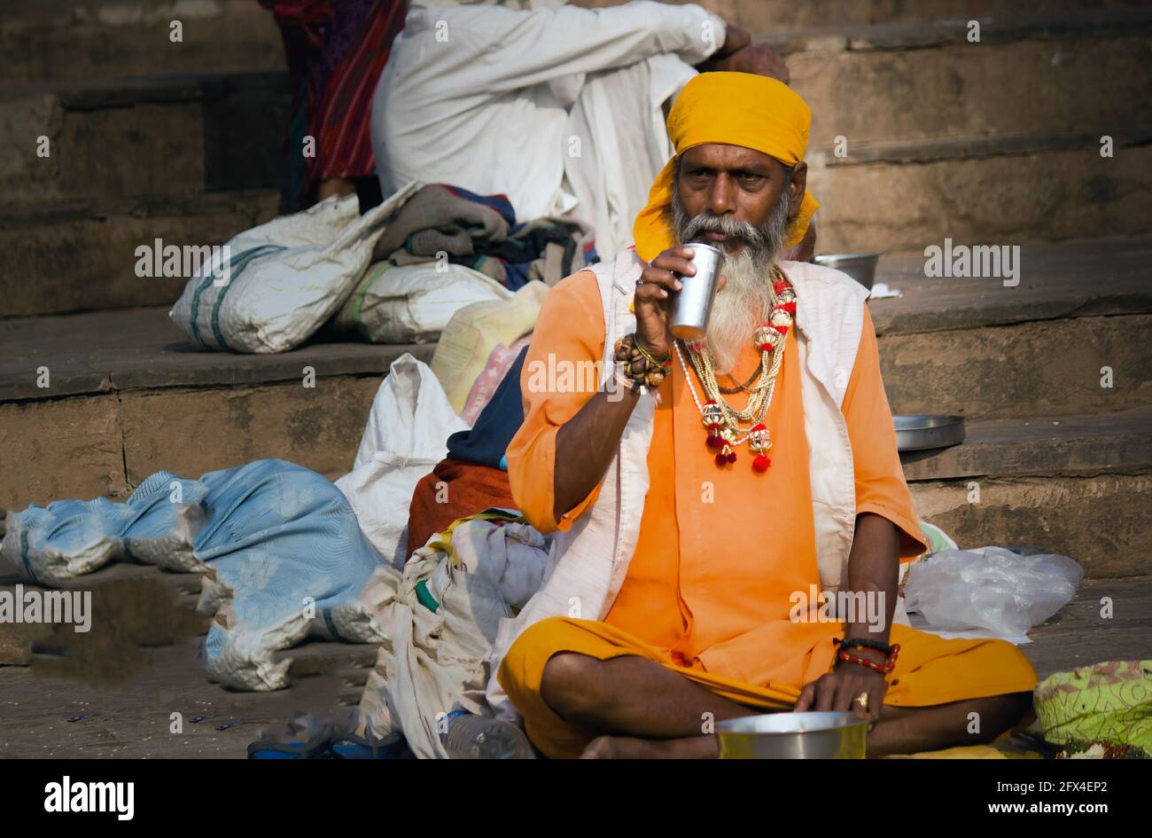 Varanasi, India - November 01, 2016: Wide angle shot of an hindu bearded sadhu, pilgrim portrait with steel glass drinking water while sitting in Hind Stock Photo