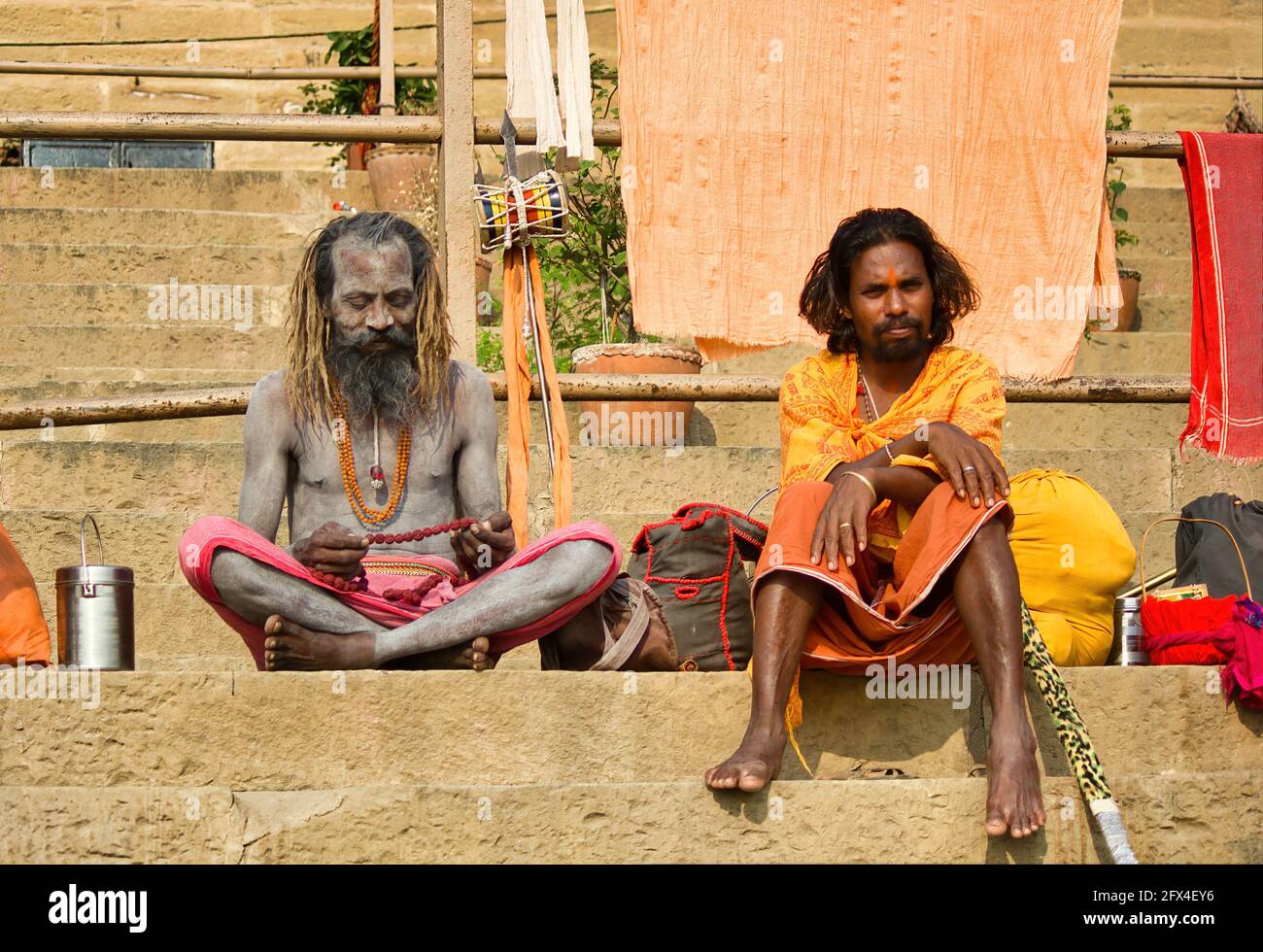 Varanasi, India - November 01, 2016: Two hindu bearded sadhu, pilgrim with damru on spear sitting in Hindu kesari orange traditional clothes in ganga Stock Photo