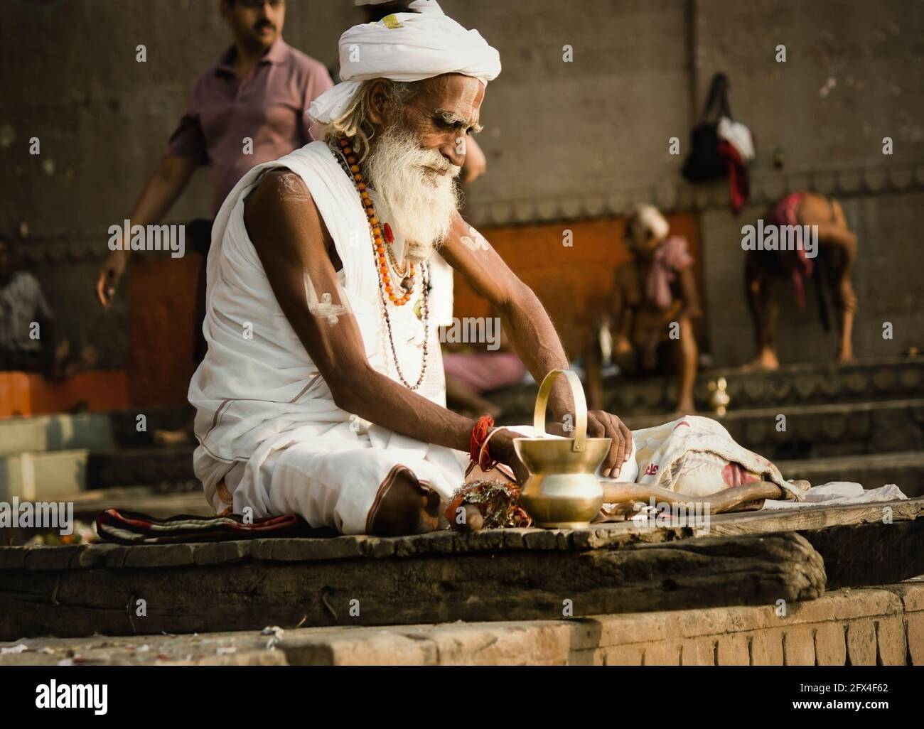Varanasi, India - November 01, 2016: Portrait of a hindu white bearded old man sadhu, pilgrim in white clothes and turban sitting with a lota on stair Stock Photo