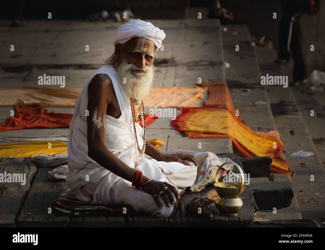 Varanasi, India - November 01, 2016: Portrait of a hindu white bearded old man sadhu, pilgrim in white clothes and turban sitting with a lota on stair Stock Photo