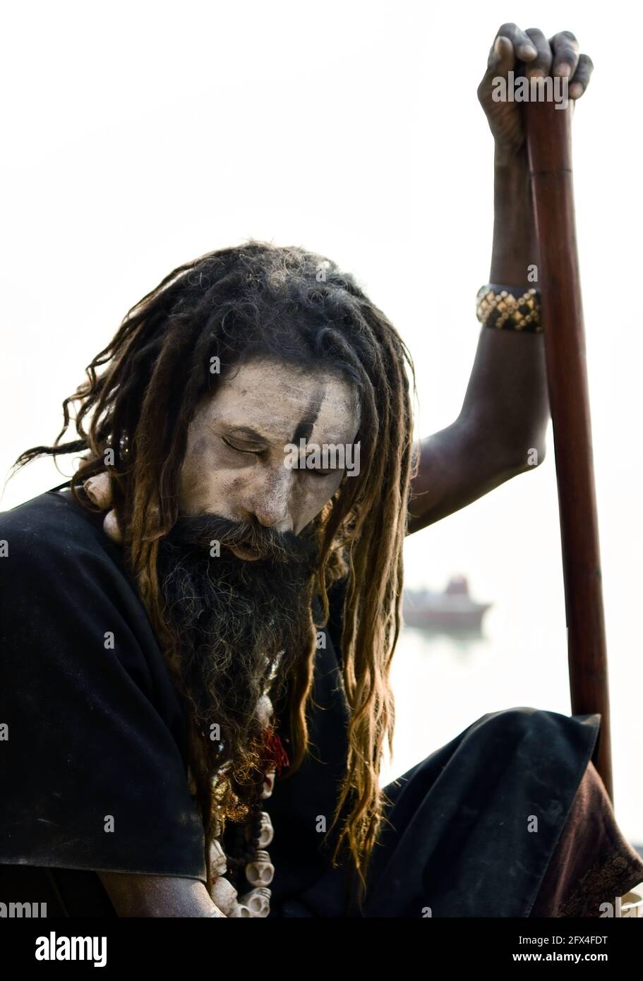 Varanasi, India - November 01, 2016: Portrait of a hindu bearded sadhu, pilgrim or Aghori baba in black cloths with closed eyes sitting with a stick a Stock Photo