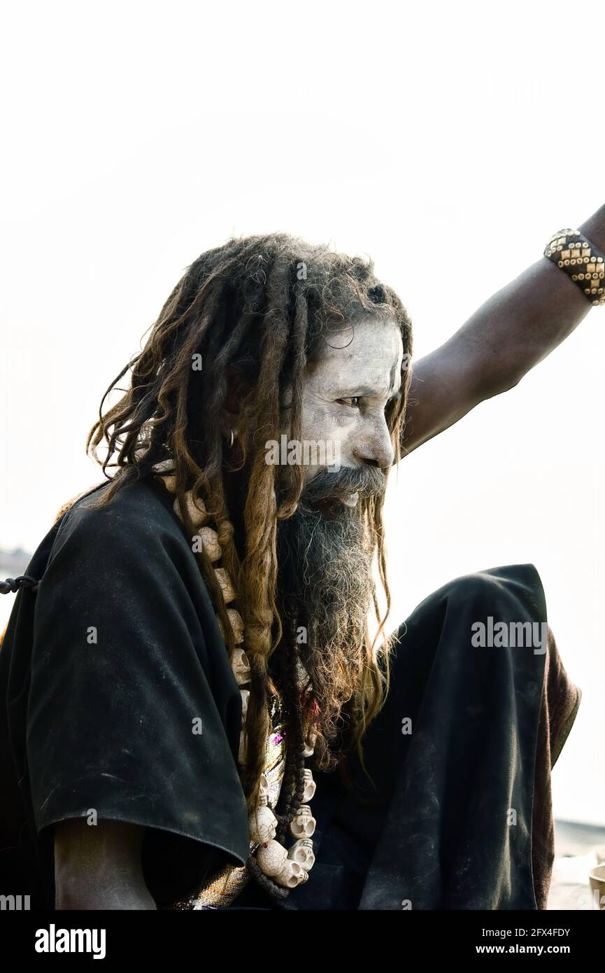 Varanasi, India - November 01, 2016: Portrait of a hindu bearded sadhu, pilgrim or Aghori baba in black cloths with closed eyes sitting with a stick a Stock Photo