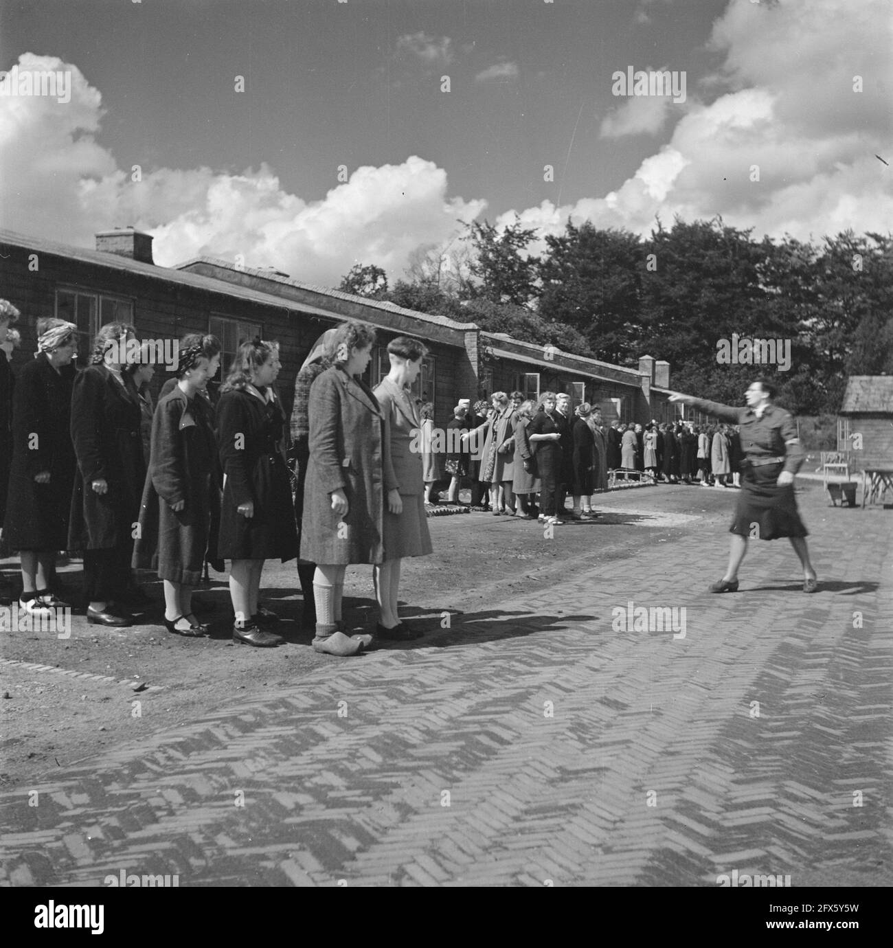Groups of women are assembled at an apple place. A camp guard gives