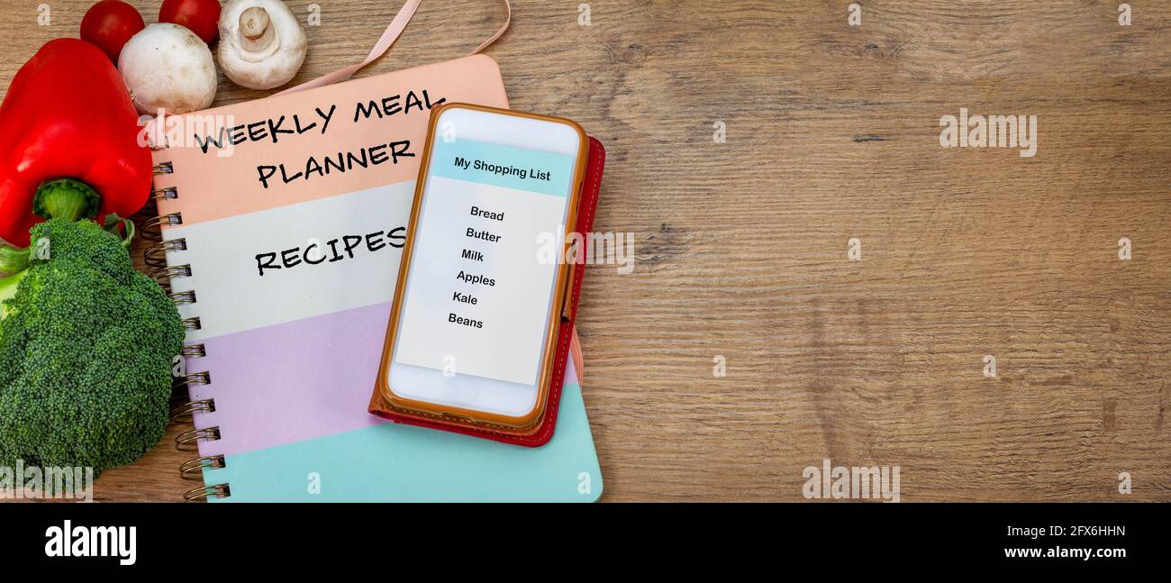 grocery shopping list on smartphone, with weekly meal planner and recipe book on counter top, fresh vegetables, plan meals and make a shopping list to Stock Photo