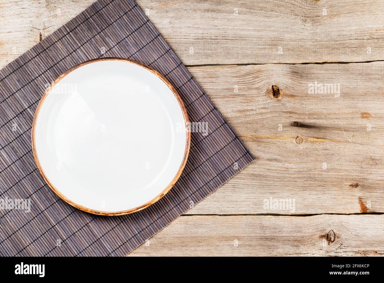 Empty white ceramic dish on rustic wooden table with brown bamboo mat Stock Photo