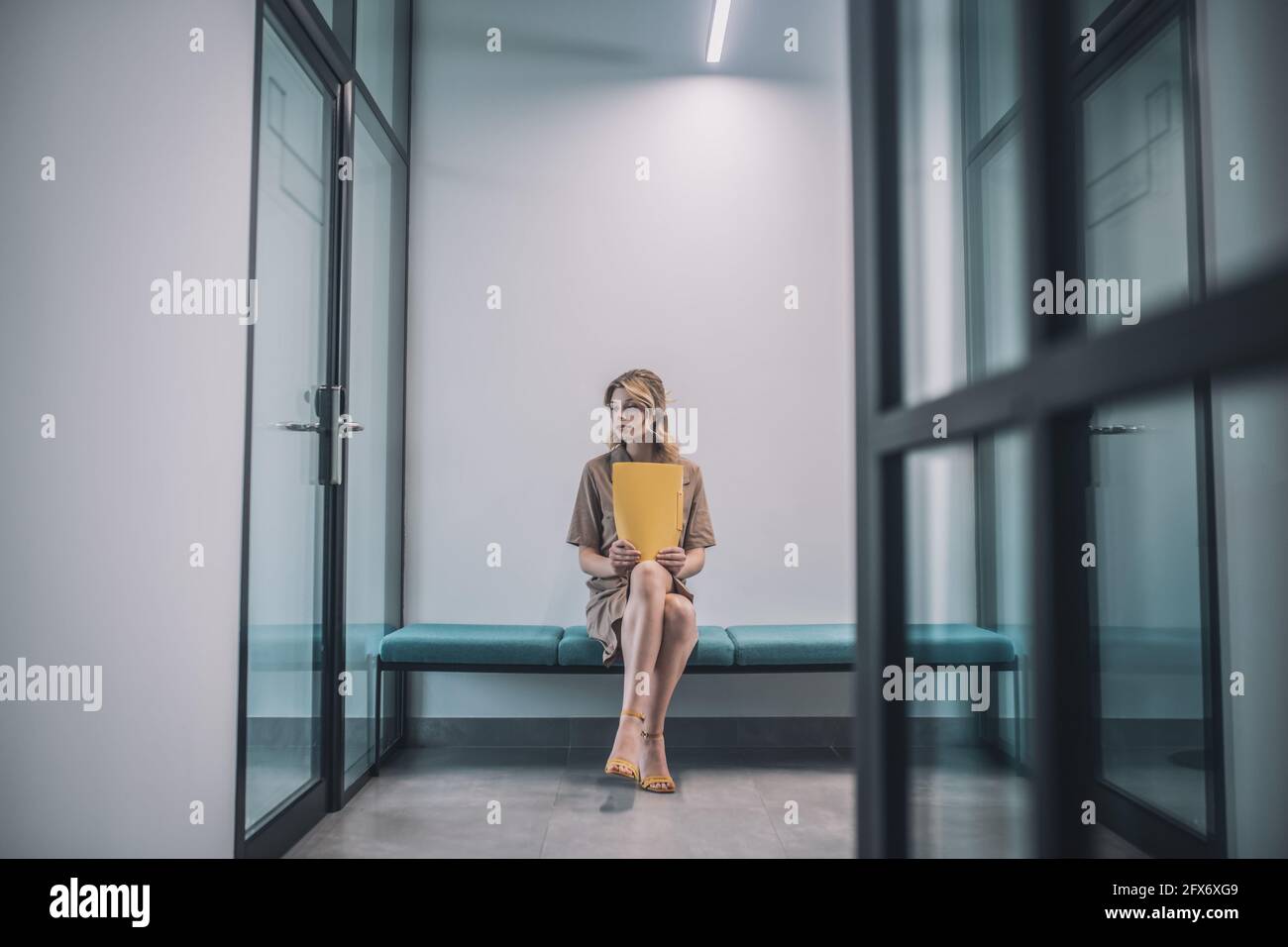 Woman in dress with folder sitting in office corridor Stock Photo