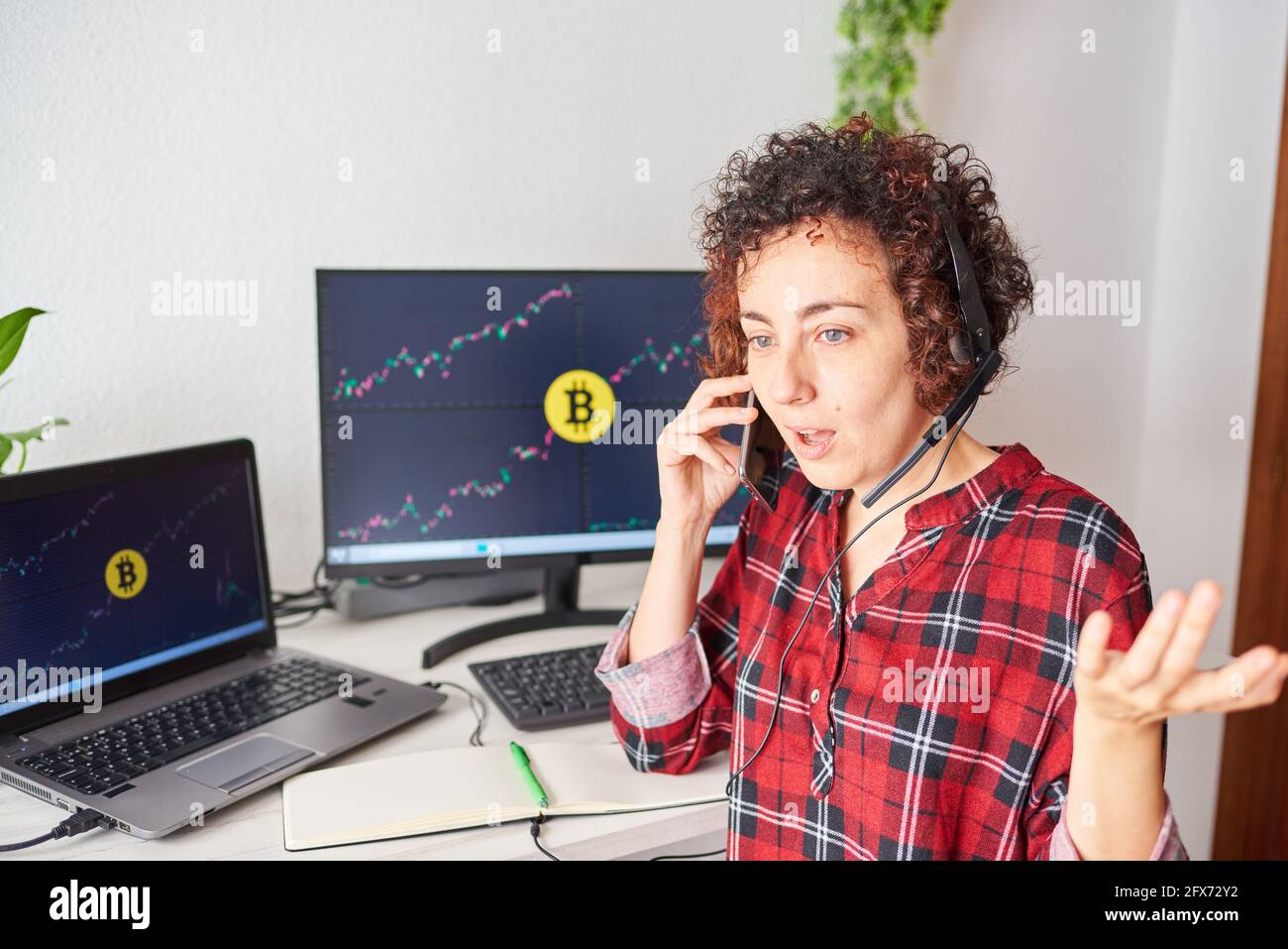 Shocked trader woman talks on the mobile phone with some screens with cryptocurrency data on her computer screens Stock Photo