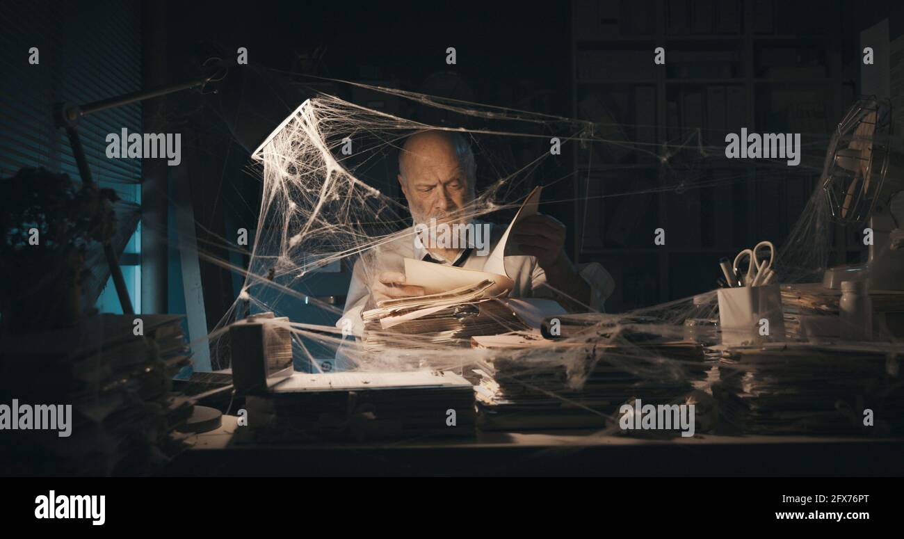 Corporate businessman searching for paperwork in an abandoned office: failure, financial crisis and outdated business concept Stock Photo