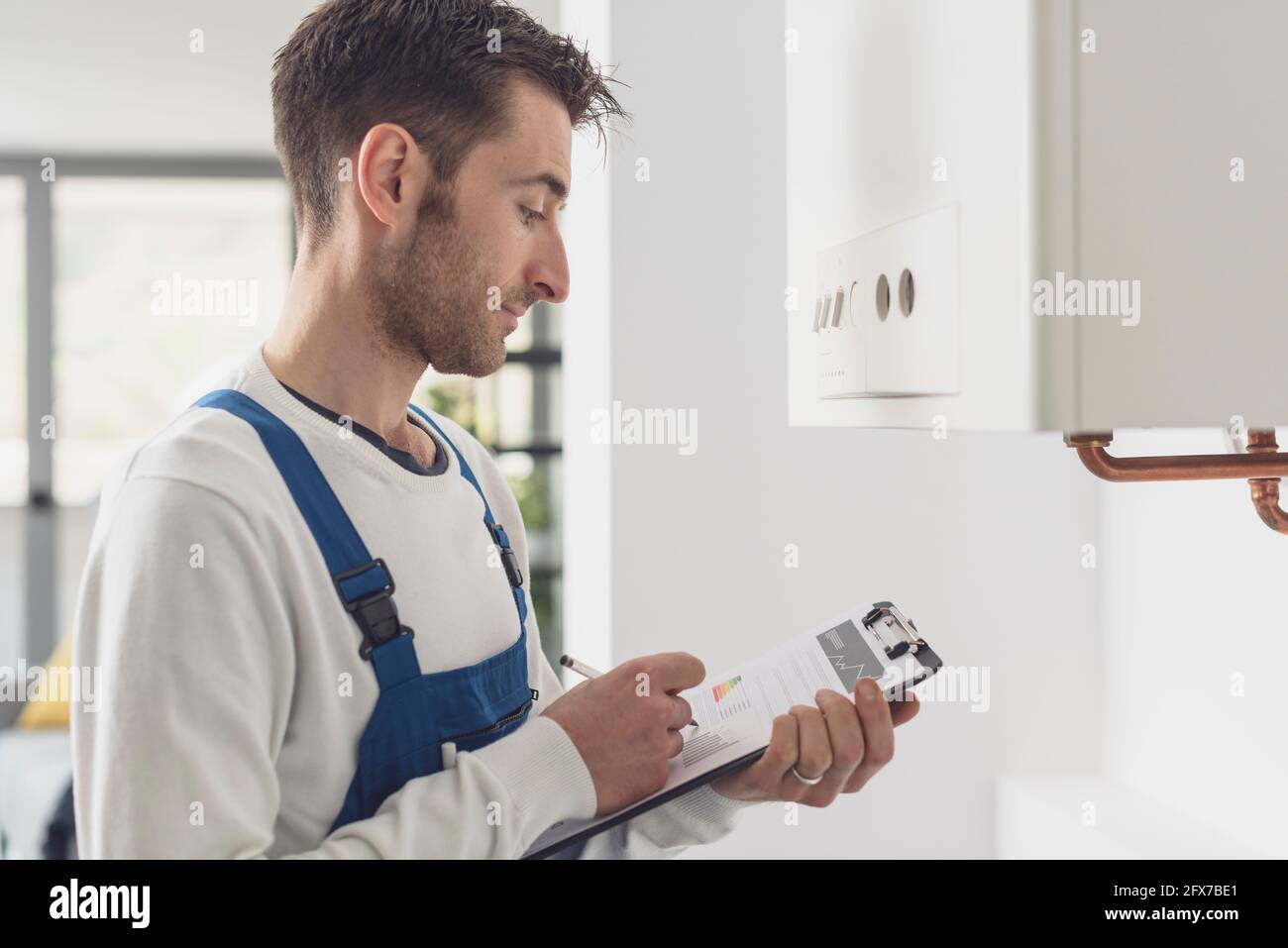 Professional plumber checking a boiler at home and writing on a clipboard Stock Photo