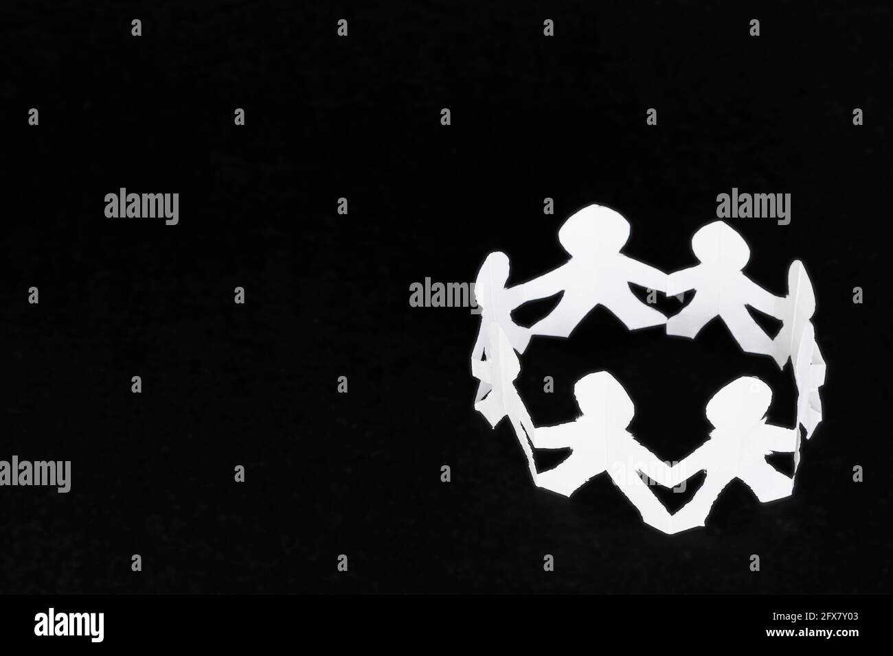 Circle of human figures made of white paper over a black surface. Stock Photo